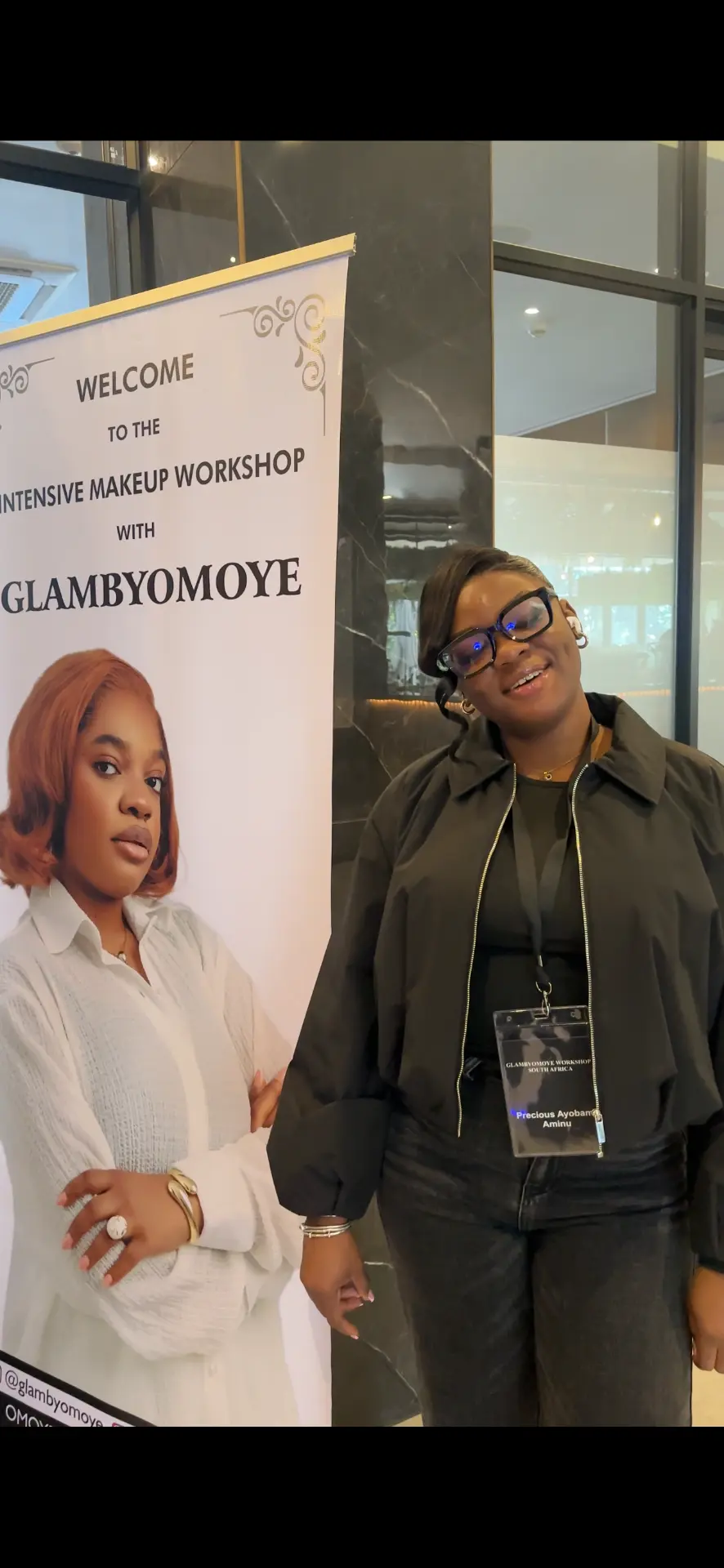 A Glam By Omoye workshop attendee beside the event welcome display